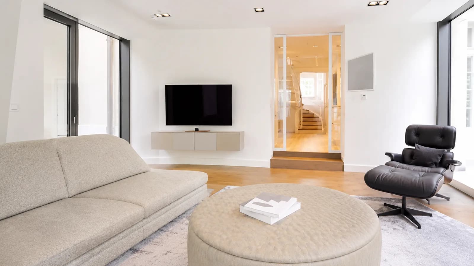 Wohnbereich mit Sofa, Loungesessel und verglastem Treppenaufgang, Hartenfels