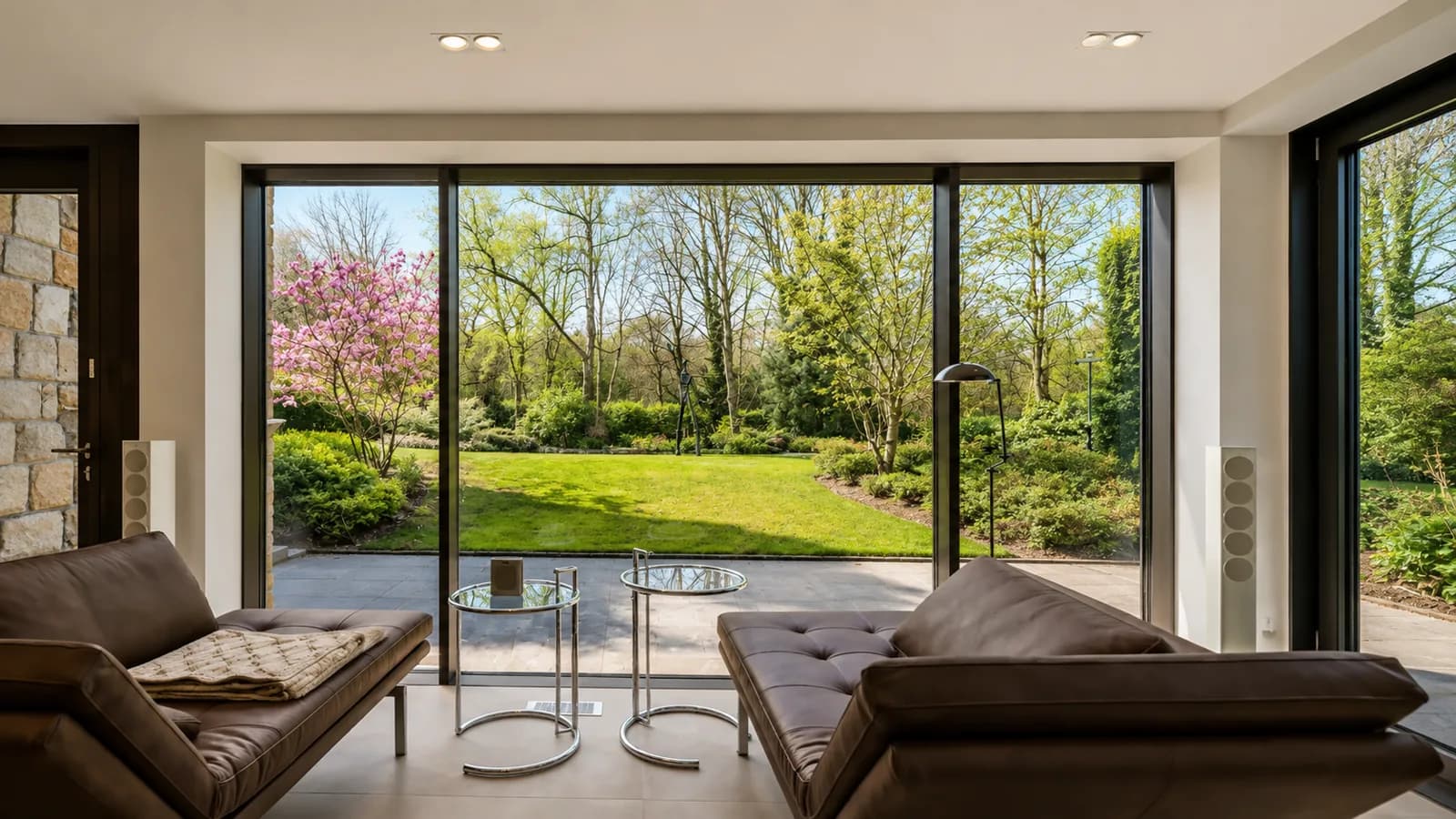 Ledersessel mit Glastischen vor der Glasfront, Blick auf die blühende Magnolie im Garten, Hartenfels