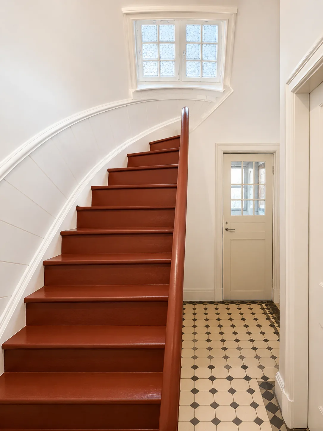 Geschwungene rot lackierte Holztreppe mit weißem Geländer über Mosaikfliesen, Hartenfels